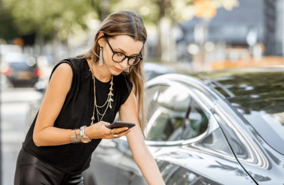 A woman charging her electric vehicle while checking her smartphone.