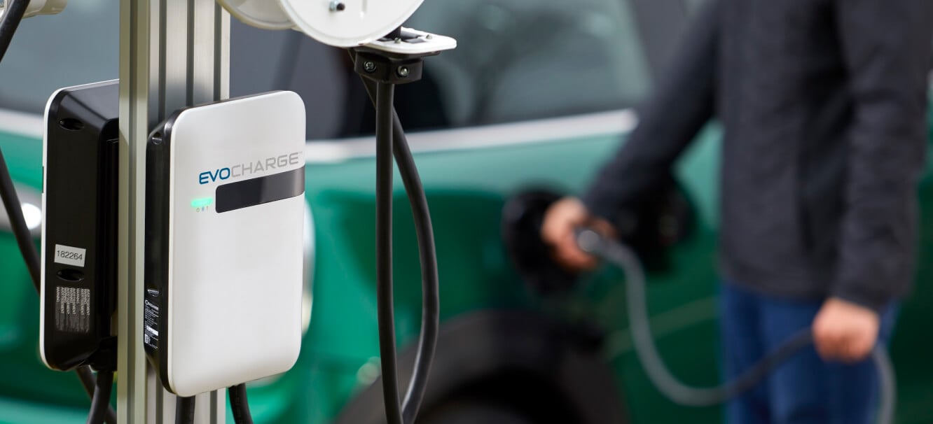 An EvoCharge charger in the forefront with a man charging his car in the background