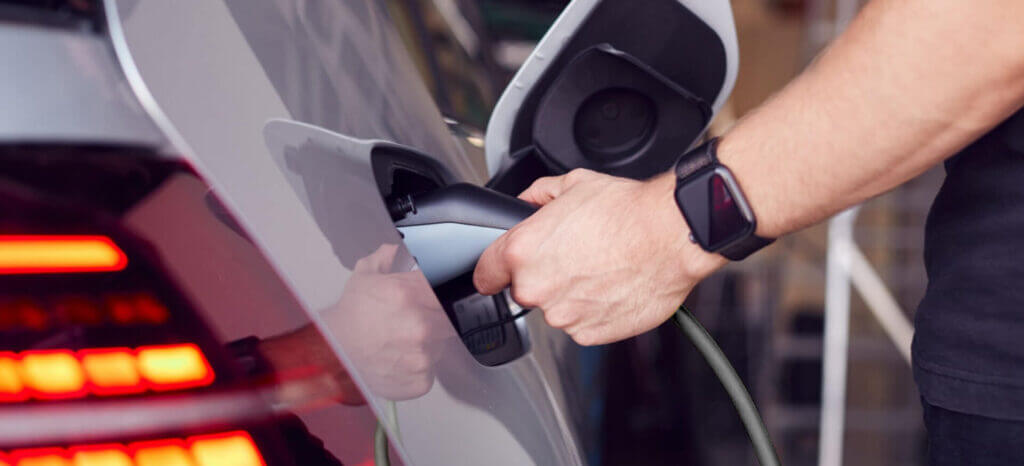 A man's hand inserting an electric charger into the charging port of his car