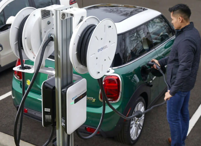 A man uses an EvoCharge charging station in an outdoor parking lot to power up his EV.