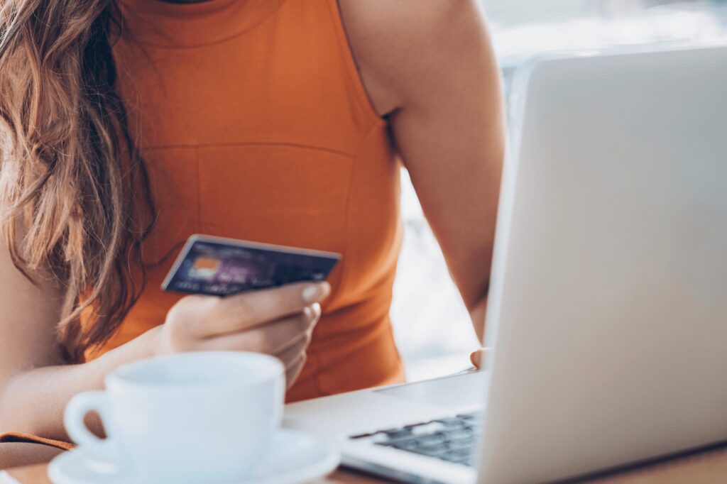 An upclose photo of a woman referencing her credit card as she types on a laptop.
